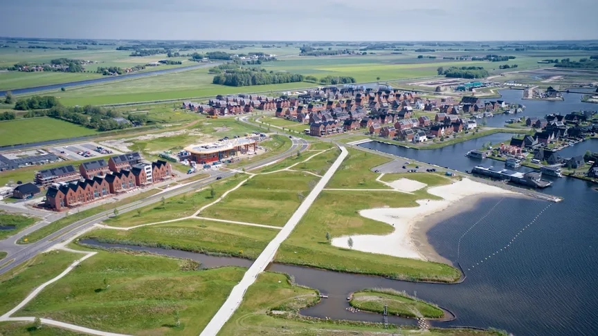 Vogelvlucht van een woonwijk en weilanden aan het water