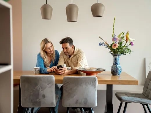 Vrouw en man zitten aan tafel met telefoon in de hand