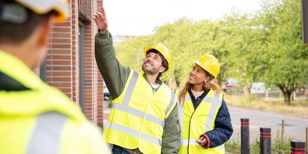 Jong koppel loopt over straat en wijst naar een nieuwbouwwoning