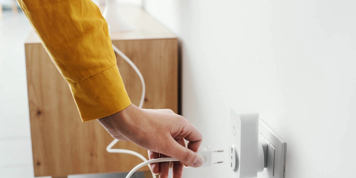 Vrouw steekt de oplader van haar mobiel in het stopcontact